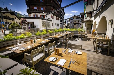 Terrasse Restaurant Neuwirt Außenterrasse eines Restaurants mit eingedeckten Holztischen, Stühlen und Blick auf alpine Gebäude.