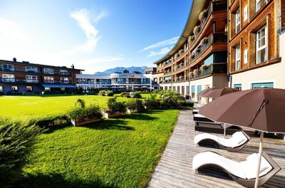 470460071 Ein Hotel mit einem schönen Garten und komfortablen Liegen. Im Hintergrund sind die Berge und ein klarer Himmel zu sehen.