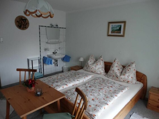Gästezimmer im Haus Alpenrose Gästezimmer mit Doppelbett aus Holz, Esstisch und Waschbecken an der Wand.