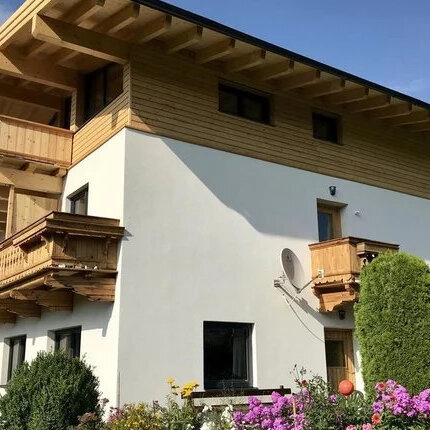 Ein modernes Landhaus mit Holzverkleidung und einem großen Balkon, umgeben von bunten Blumen und grünen Sträuchern.