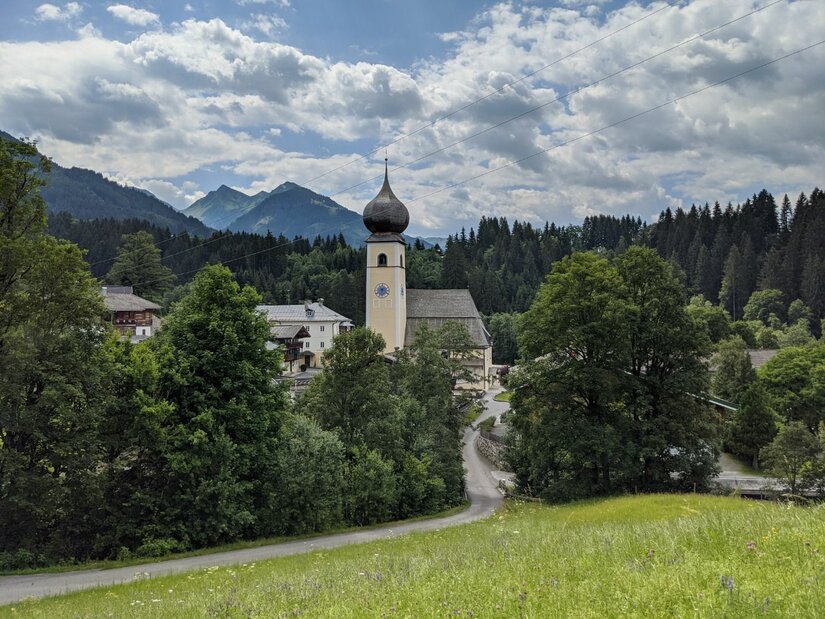 Pfarrkirche Aurach bei Kitzbühel Kirche mit Zwiebelturm in Aurach vor bewaldeten Bergen und bewölktem Himmel.