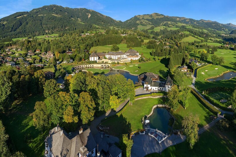 Golfclub Kitzbühel Luftaufnahme eines Golfplatzes mit Clubhaus, Teichen und bewaldeten Bergen im Hintergrund.