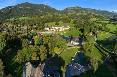 Golfclub Kitzbühel Luftaufnahme eines Golfplatzes mit Clubhaus, Teichen und bewaldeten Bergen im Hintergrund.