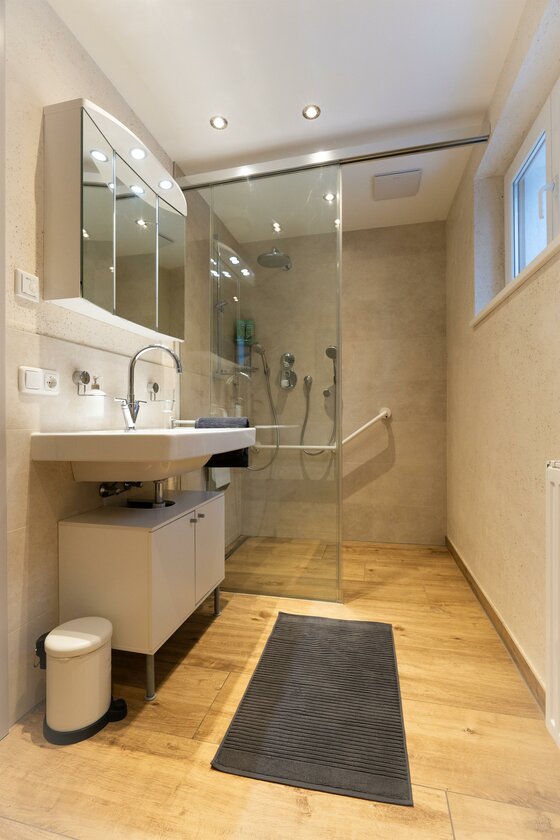 Ein modernes Badezimmer mit einer Glasdusche und einem Doppelwaschbecken. Der Boden ist aus Holz und es gibt ein großes Fenster.