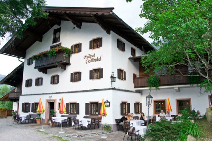 Außenansicht des Gasthofs Jodlbühel mit weißer Fassade, dunklen Fensterläden und einer Terrasse mit Gästen.