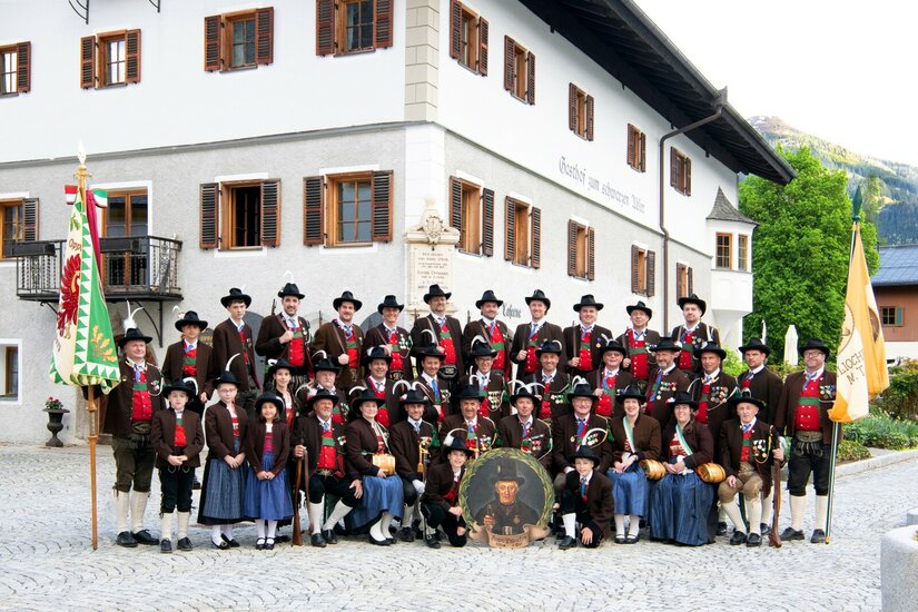 Eine große Gruppe von Personen in traditioneller Tiroler Schützentracht posiert vor einem historischen Gasthof.
