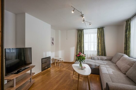 Wohnzimmer mit grauem Ecksofa, weißem Couchtisch, Fernseher und Kaminofen auf Parkettboden.
