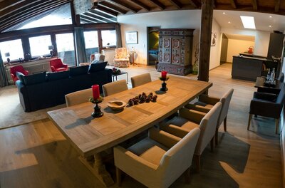 RÉSIdence Reith Kitzbühel Innenansicht Moderner Wohn- und Essbereich mit großem Holztisch, dunklem Sofa und rustikalem Schrank unter einer Dachschräge.