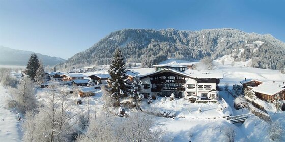 Aussenansicht Hotel Zimmermann Verschneites Hotel Zimmermann in einer alpinen Winterlandschaft mit bewaldeten Bergen im Hintergrund.