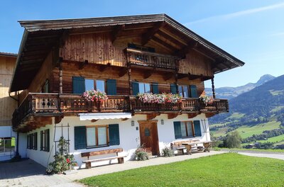 Ferienwohnung Schatzhof Traditionelles Alpenhaus aus Holz und Stein mit Blumenbalkonen vor Gebirgspanorama.