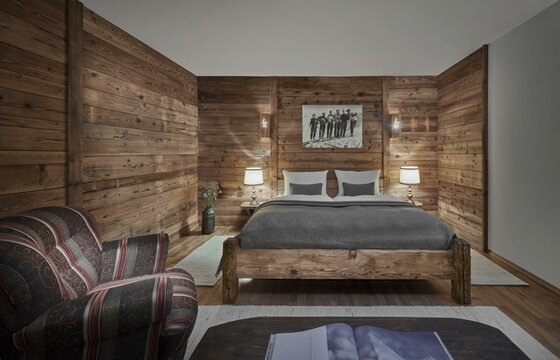 Hotel Goldener Greif Doppelbettzimmer Doppelbett aus Holz in einem Zimmer mit Holzwänden, Nachttischlampen und einem gemusterten Sessel.