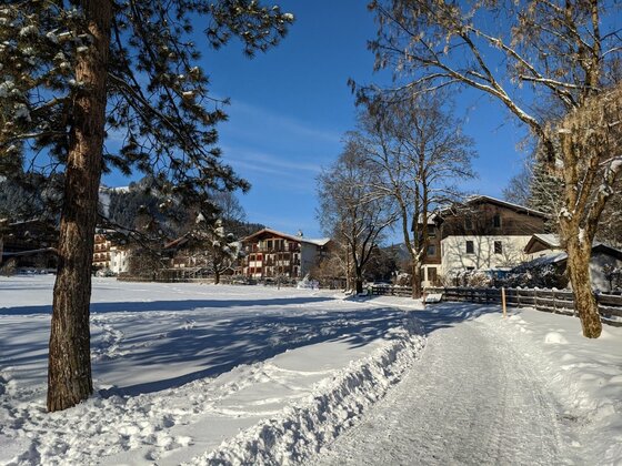 Winterwanderweg am Schwarzsee Verschneiter Wanderweg führt an alpinen Häusern und Bäumen unter blauem Himmel vorbei.