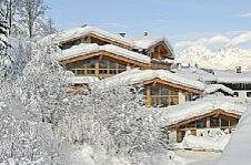 Ehrenbachhof im Winter Verschneite Holzchalets mit schneebedeckten Dächern und Bäumen vor Gebirgskulisse.