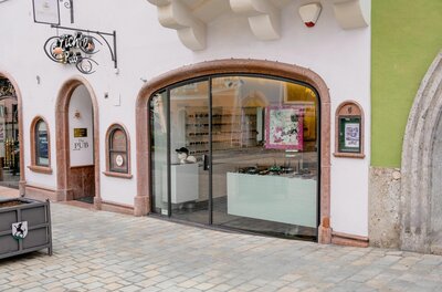 Meikl Optik in der Altstadt Schaufenster eines Optikergeschäfts mit Rundbogen in einer gepflasterten Fußgängerzone.