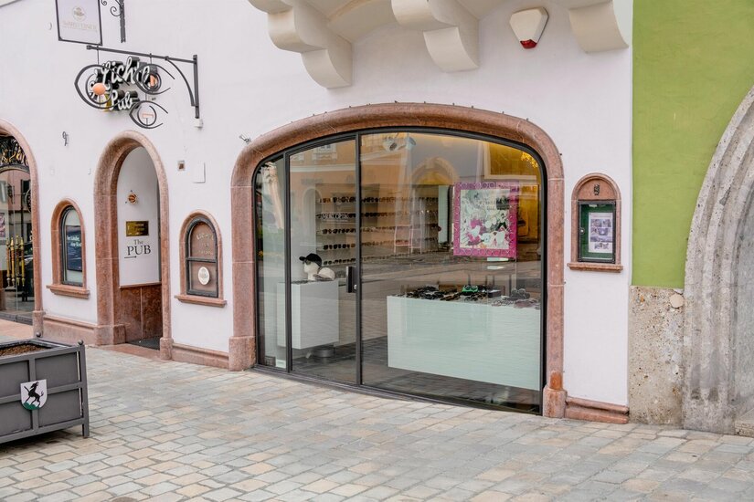 Meikl Optik in der Altstadt Schaufenster eines Optikergeschäfts mit Rundbogen in einer gepflasterten Fußgängerzone.