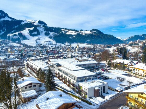Rehaklinik Kitzbühel im Winter Luftaufnahme der Rehaklinik Kitzbühel und des verschneiten Ortes vor bewaldeten Bergen.