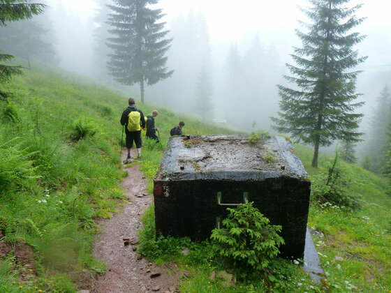 Wanderweg bei der Seidlalm Wanderer auf einem schmalen Pfad im Nebel neben einem Betonbauwerk.