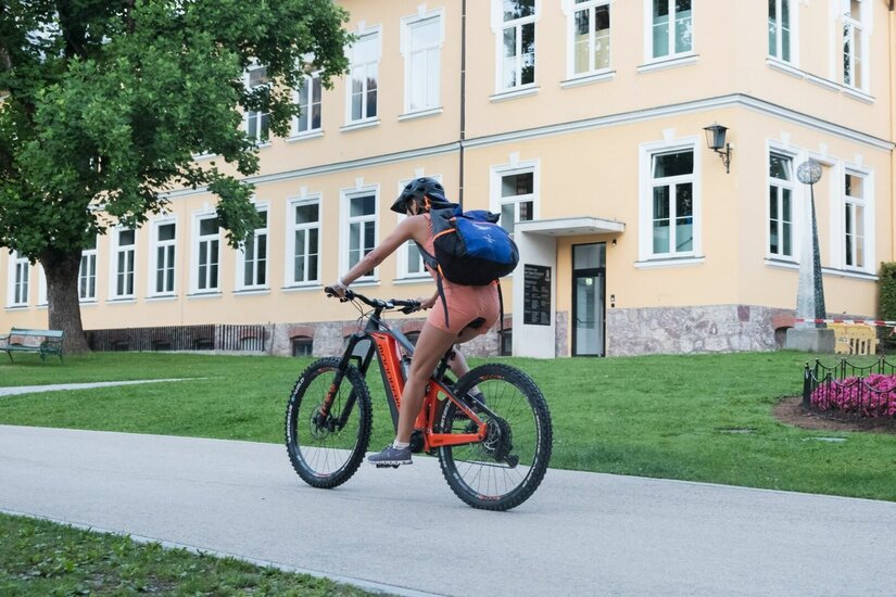 Radfahrerin vor historischem Gebäude Eine Frau fährt mit einem Mountainbike auf einem asphaltierten Weg vor einem gelben Gebäude.