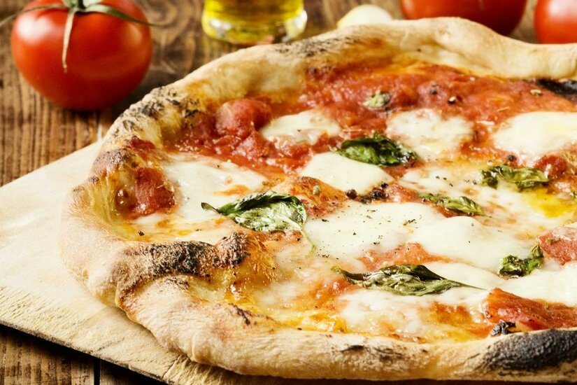 Pizza Eine frisch gebackene Pizza mit Mozzarella, Tomatensauce und frischem Basilikum. Im Hintergrund sind frische Tomaten und Olivenöl zu sehen.