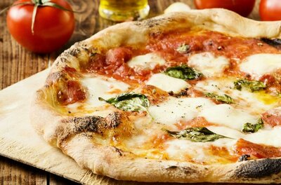 Pizza Eine frisch gebackene Pizza mit Mozzarella, Tomatensauce und frischem Basilikum. Im Hintergrund sind frische Tomaten und Olivenöl zu sehen.