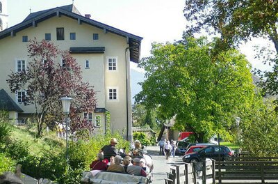 Pfarrhof Eine ruhige Straße mit einem großen Gebäude im Hintergrund. Menschen sitzen in einem offenen Fahrzeug und genießen die Landschaft.