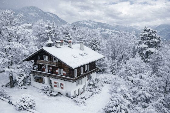 Ein hübsches Haus im Winter, umgeben von schneebedeckten Bäumen. Der Himmel ist grau und die Landschaft sieht friedlich aus.