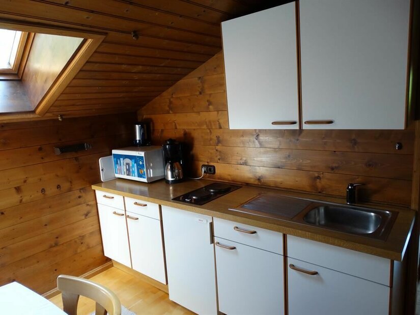 Küche im Haus Lindler Kleine Küchenzeile mit weißen Fronten unter einer Holzschräge mit Dachfenster.