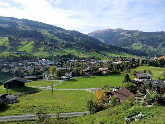 Dorfpanorama am Schützkogel Alpinsteig Blick auf ein Dorf im Tal mit grünen Wiesen und bewaldeten Bergen im Hintergrund.