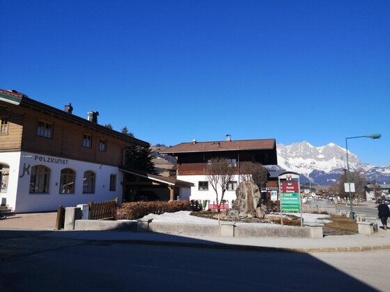 Alpiner Ort mit traditionellen Holzhäusern vor schneebedeckten Bergen unter blauem Himmel.