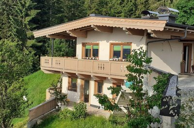 Zweistöckiges Gebäude mit Holzfassade und Balkon vor einem Nadelwald.