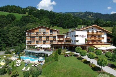 Außenansicht des Hotels Bichlhof mit Außenpool, Liegewiese und bewaldeten Bergen im Hintergrund.