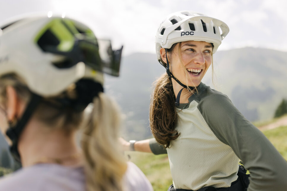 In Kitzbühel, a cyclist wearing a helmet is enjoying the mountain scenery and chatting with friends.