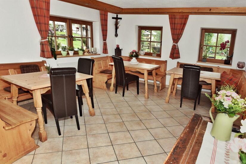 Gastraum im Astlingerhof Rustikaler Gastraum mit Holztischen, Eckbänken und dunklen Lederstühlen auf Fliesenboden.