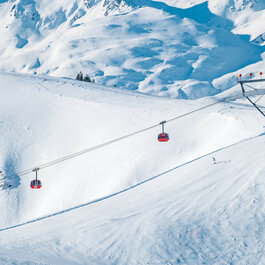 The red 3S gondola in the Kitzbühel ski area glides over snow-covered slopes as skiers make their way down the runs.