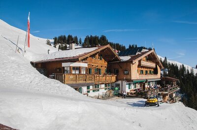 Melkalm Winteransicht Alpiner Berggasthof aus Holz in einer verschneiten Winterlandschaft unter blauem Himmel.