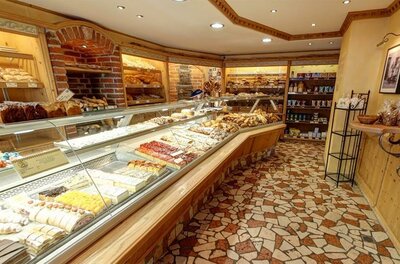 Innenansicht einer Bäckerei mit Glastheke voller Kuchen und Brotregalen im Hintergrund.
