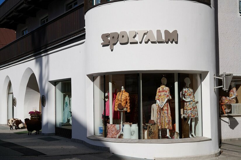 Sportalm Kitzbühel Ladengeschäft Außenansicht eines Bekleidungsgeschäfts mit Schaufenstern und dem Schriftzug Sportalm an einer weißen Fassade.
