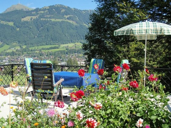 Terrasse Haus Kolb Sonnenterrasse mit Gartenmöbeln, Blumenbeeten und Blick auf bewaldete Berge und ein Tal.