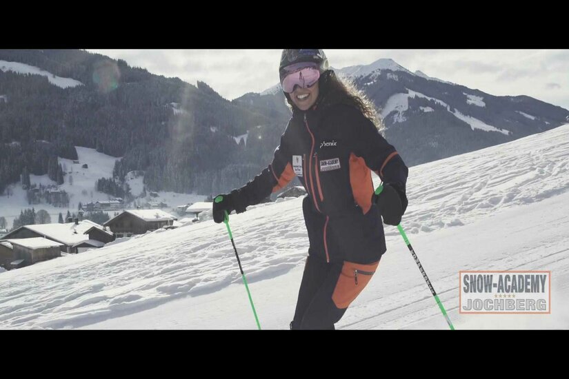 Snow Academy Jochberg Skifahrerin in dunkler Skikleidung auf einer verschneiten Piste vor Bergpanorama.