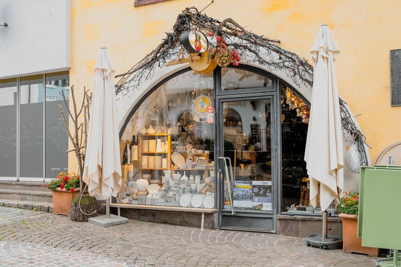 Tutto Italia Ladengeschäft Eingangsbereich eines Geschäfts mit Rundbogenfenster, Keramikwaren im Schaufenster und zwei weißen Sonnenschirmen.