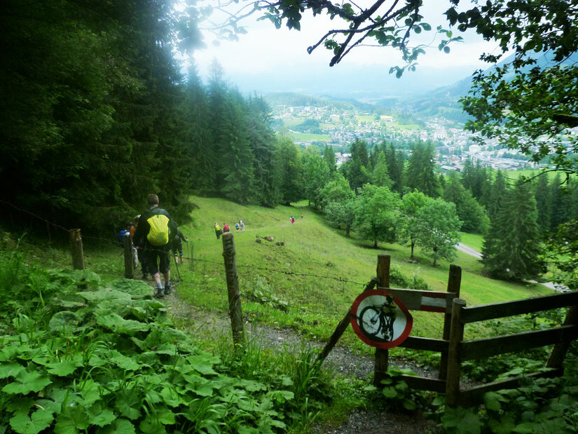 Wanderweg bei der Seidlalm Wanderer auf einem schmalen Pfad neben einem Holzzaun mit Blick auf eine Wiese und ein Tal.