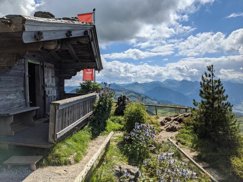 Hütte am Kitzbüheler Horn Rustikale Holzhütte mit Terrasse vor einem Bergpanorama unter bewölktem Himmel.