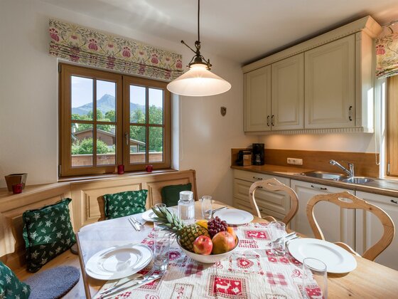 Küche im Appartement Hahnenkamm Rustikale Küche mit Esstisch, Eckbank und Blick durch das Fenster auf die Berge.