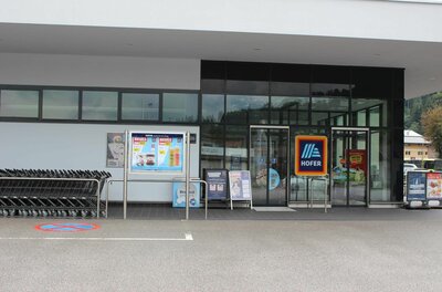 Eingangsbereich eines Hofer Supermarktes mit Glasfront, Einkaufswagen und Werbeplakaten.
