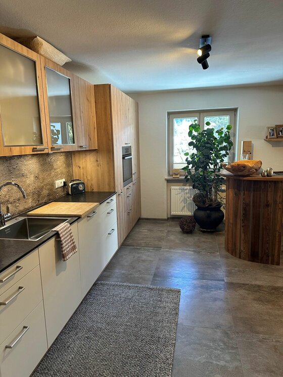 Küche im Haus Egger Moderne Einbauküche mit Holzfronten, dunkler Arbeitsplatte und einem runden Holztresen.