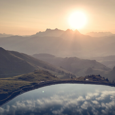 Die Sonne geht über einer malerischen Berglandschaft auf, während sich die Farben des Himmels im ruhigen Wasser spiegeln.