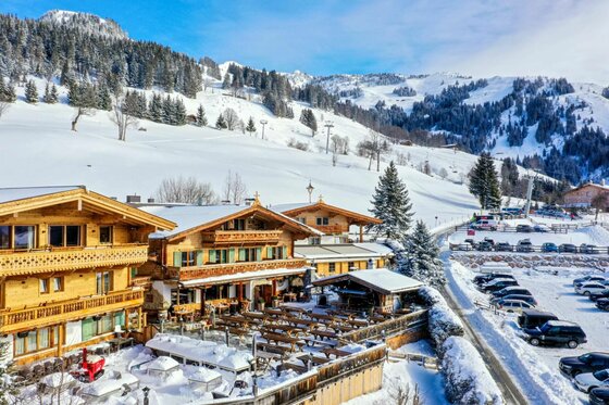 Sonnbergstuben im Winter Verschneite Holzhütten mit Außenterrasse vor bewaldeten Berghängen im Winter.