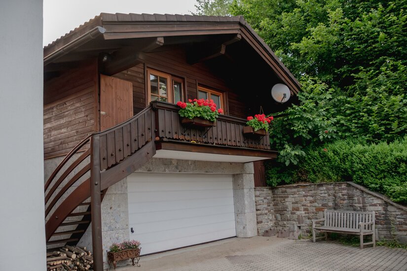 Zweistöckiges Holzhaus mit Balkon über einer Garage und einer Holztreppe im Außenbereich.