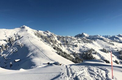 Verschneite Berglandschaft mit Skispuren im Vordergrund und Blick auf den Hochetzkogel unter blauem Himmel.