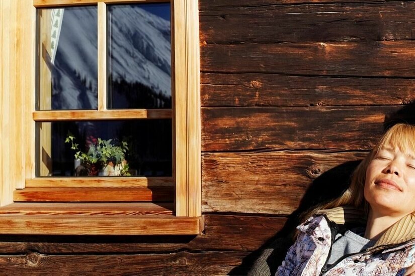 Rast an der Moseralm Ein Paar lehnt mit geschlossenen Augen an einer dunklen Holzwand einer Berghütte in der Sonne.